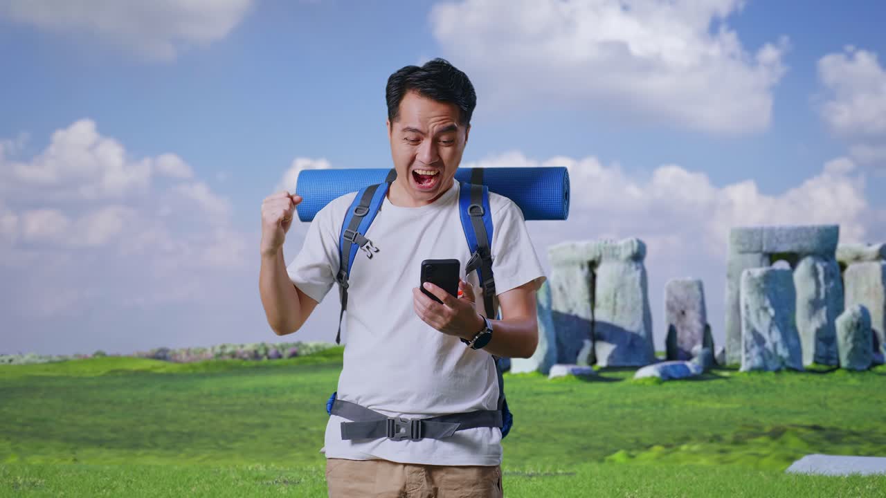 Asian Male Hiker With Mountaineering Backpack Looking At The Smartphone And Screaming Goal Celebrating The Success While Traveling In Stonehenge