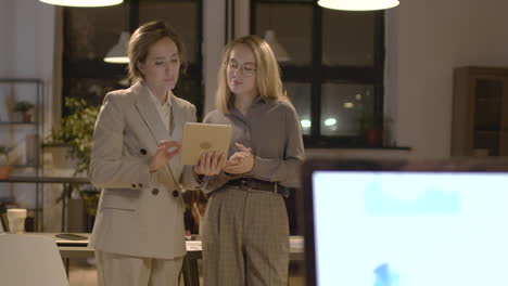 two female coworkers talking and watching a tablet standing in the office 2