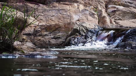 Shiny-clear-water-stream-flowing-peaceful-among-beige-rocks,-low-angle