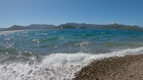 amplia vista de botes y pequeñas olas rompiendo en la costa pedregosa en verano - karaka point, queen charlotte sound