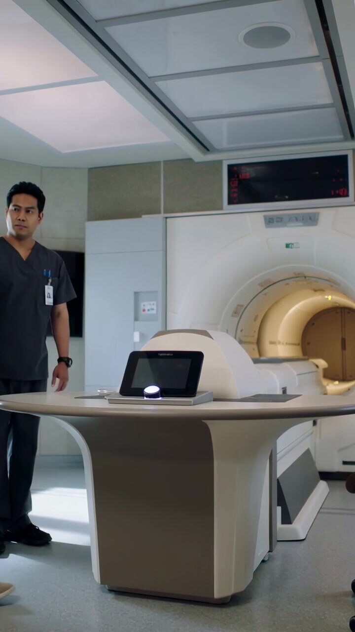 Video verticale: Tecnico in camice blu entra e usa la console nella sala MRI, mentre un uomo prepara la scansione