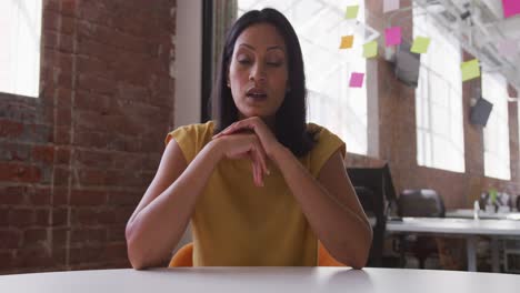 mujer de negocios de raza mixta sentada en un escritorio en la sala de reuniones haciendo una videollamada