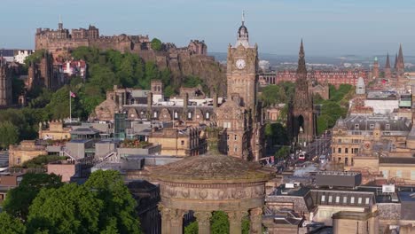 a drone dronie shot starts at the dugald stewart monument and ascends, revealing panoramic views of edinburgh cityscape under clear skies