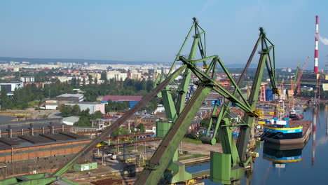 drone shot of old container harbor with rusty cranes in gdansk,poland during sunny day - cityscape in background