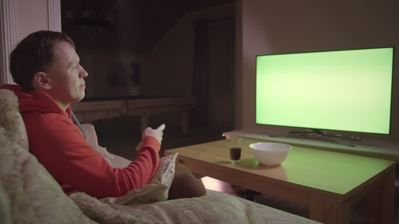 Mand ser tv og skifter kanaler, siddende i sofaen derhjemme om aftenen, kromakey.