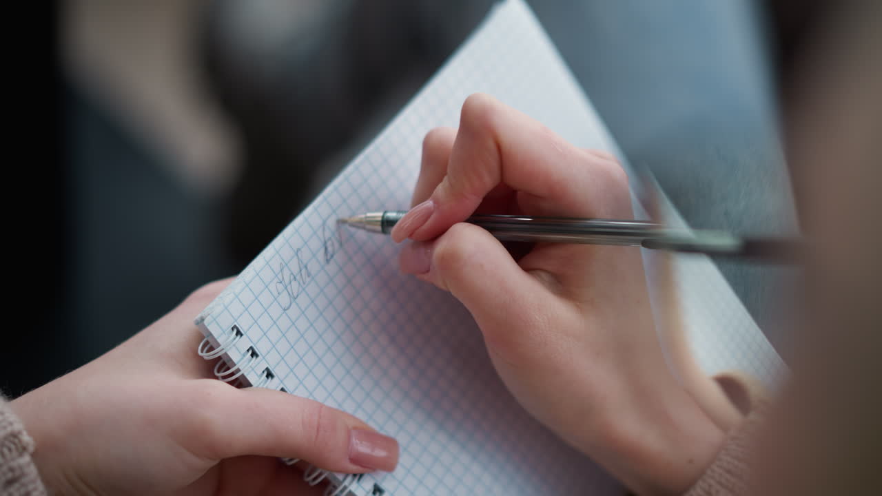 Close-up hand view of lady writing in notebook with pen, focusing on fingers and pen on graph paper, detailed close-up of writing process, female hand showing graceful writing technique
