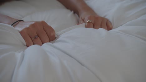 womans hands gripping white bed sheet tightly