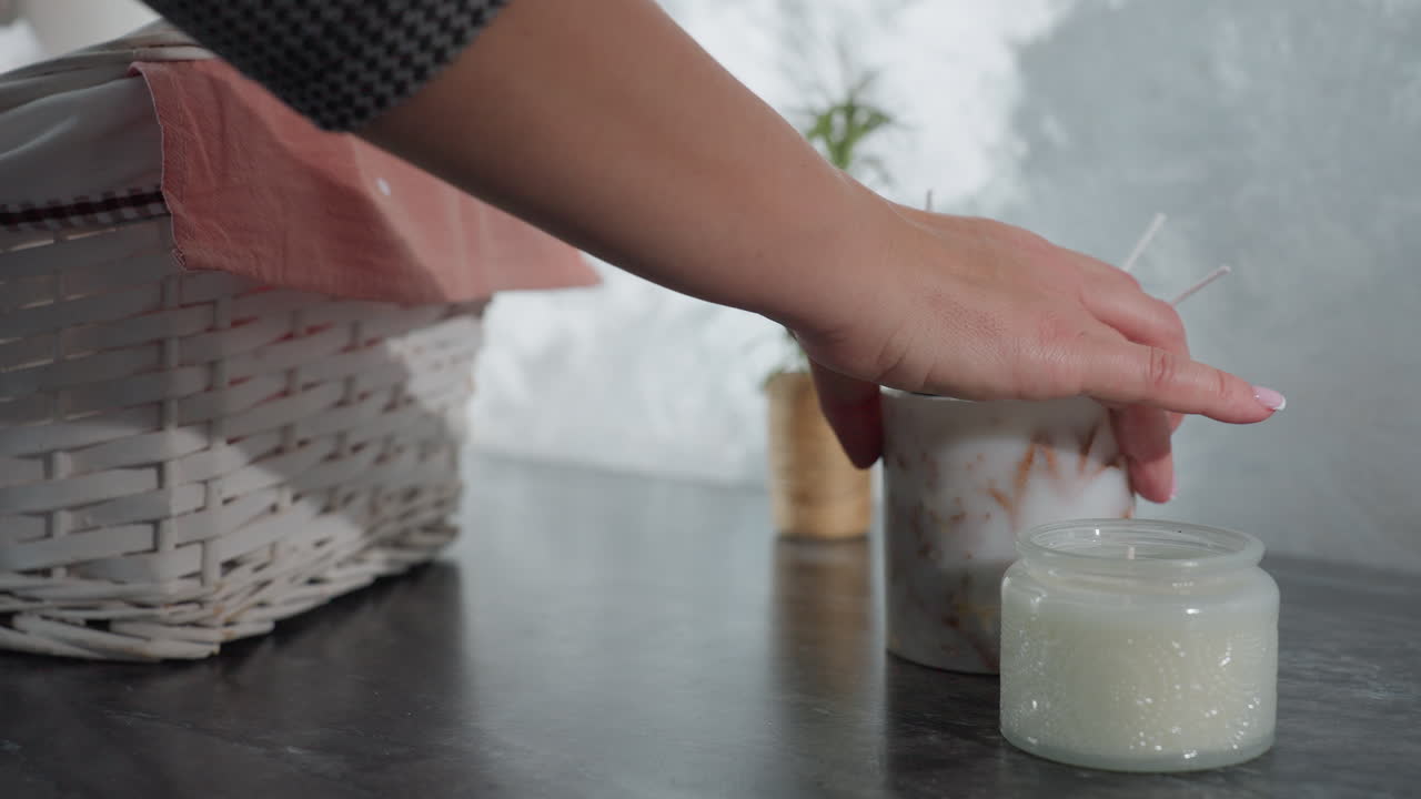 Close-up of individual dropping shopping item on marble table with wicker basket covered with pink cloth, small potted plant, and decorative white candle