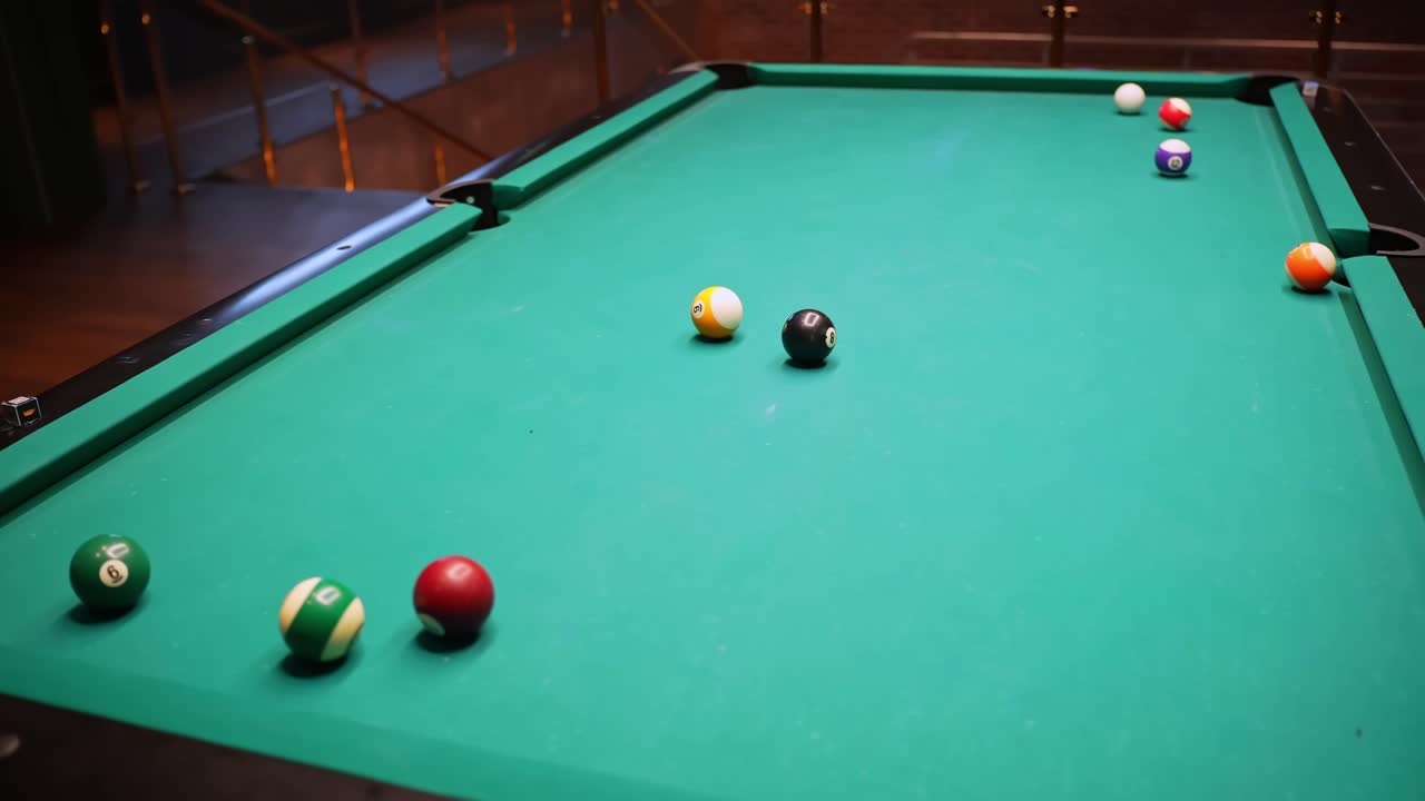 Wide view of pool table in a bar with scattered balls and player cue after a missed shot, green felt background and copy space for leisure, competition, and nightlife concepts