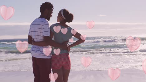 Animation-of-pink-hearts-over-happy-african-american-couple-embracing-on-beach