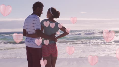 animation of pink hearts over happy african american couple embracing on beach