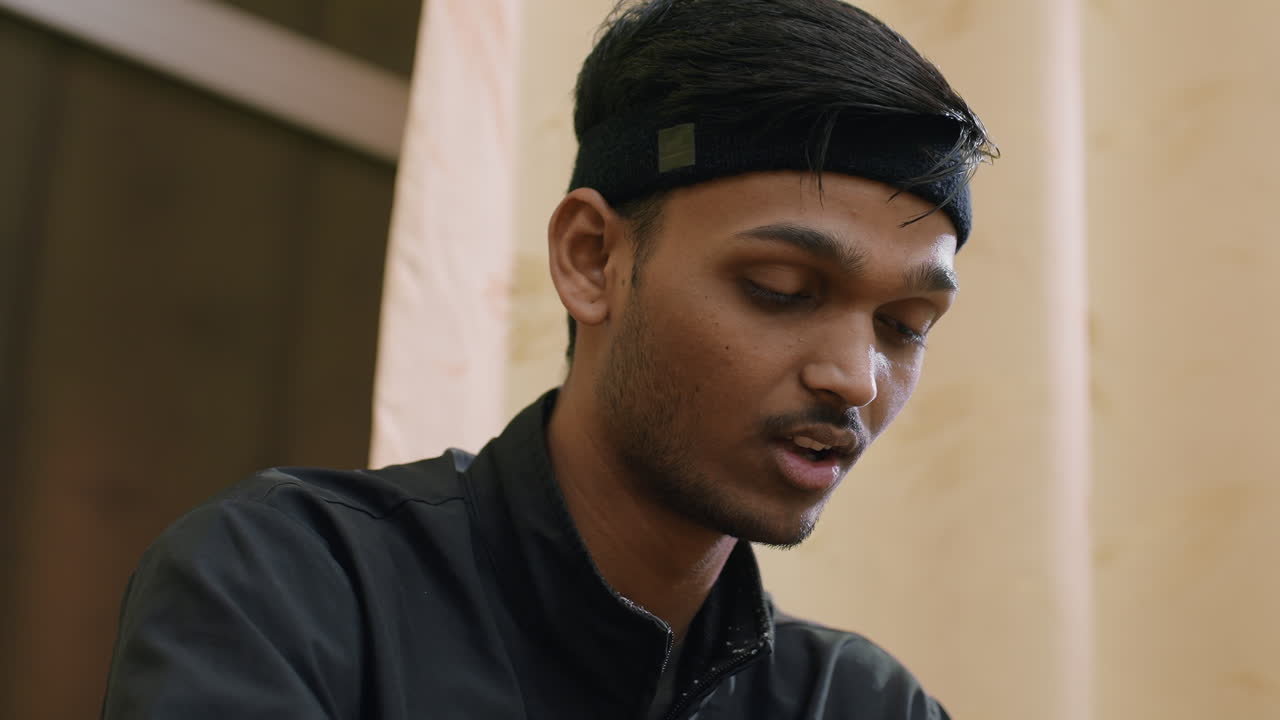 Close up of tired athlete in black sportswear with head bowed, gradually lifting up after intense indoor training, showing exhaustion, recovery, and discipline during demanding practice session