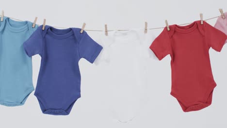 Video-of-multi-coloured-baby-grows-hanging-on-pegs-from-line-with-copy-space-on-white-background