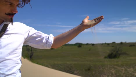 man portraying poet sandor petofi drops sand into wind on sand dune