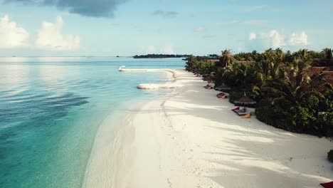 Drone-video-of-a-tropical-resort-in-the-Maldives,-low-flight,-blue-lagoon,-green-palms,-sunny-weather,-turquoise-shallow-water,-colorful-sunbeds,-4K