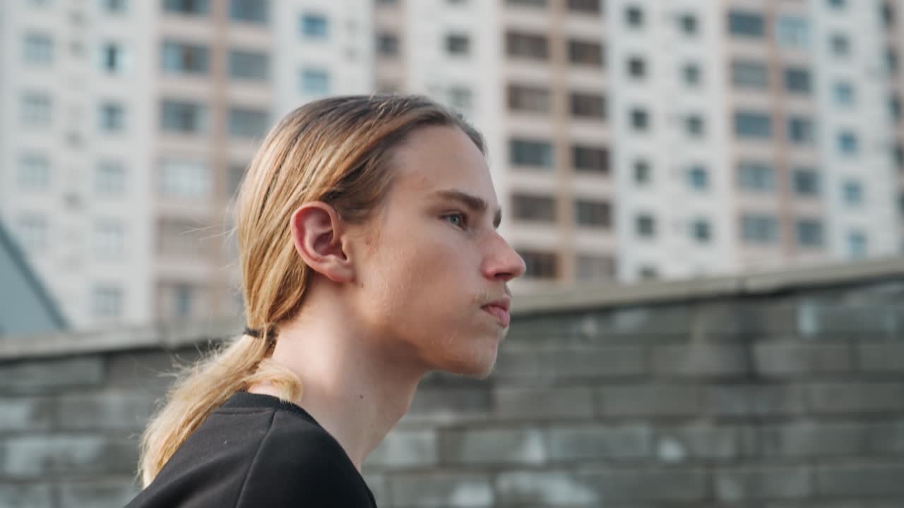 Rooftop portrait white teen gazing across city skyline, thoughtful expression, leaning on concrete ledge, apartment towers blurred, cool evening light, black sweater, low ponytail, urban solitude