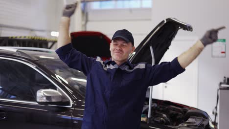 smiling mechanic man in uniform and gloves dancing funny in a modern service auto center