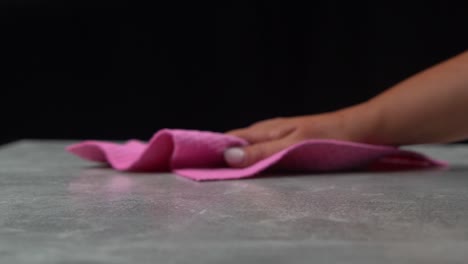 woman uses pink cloth to clean up mess made on grey table with black background