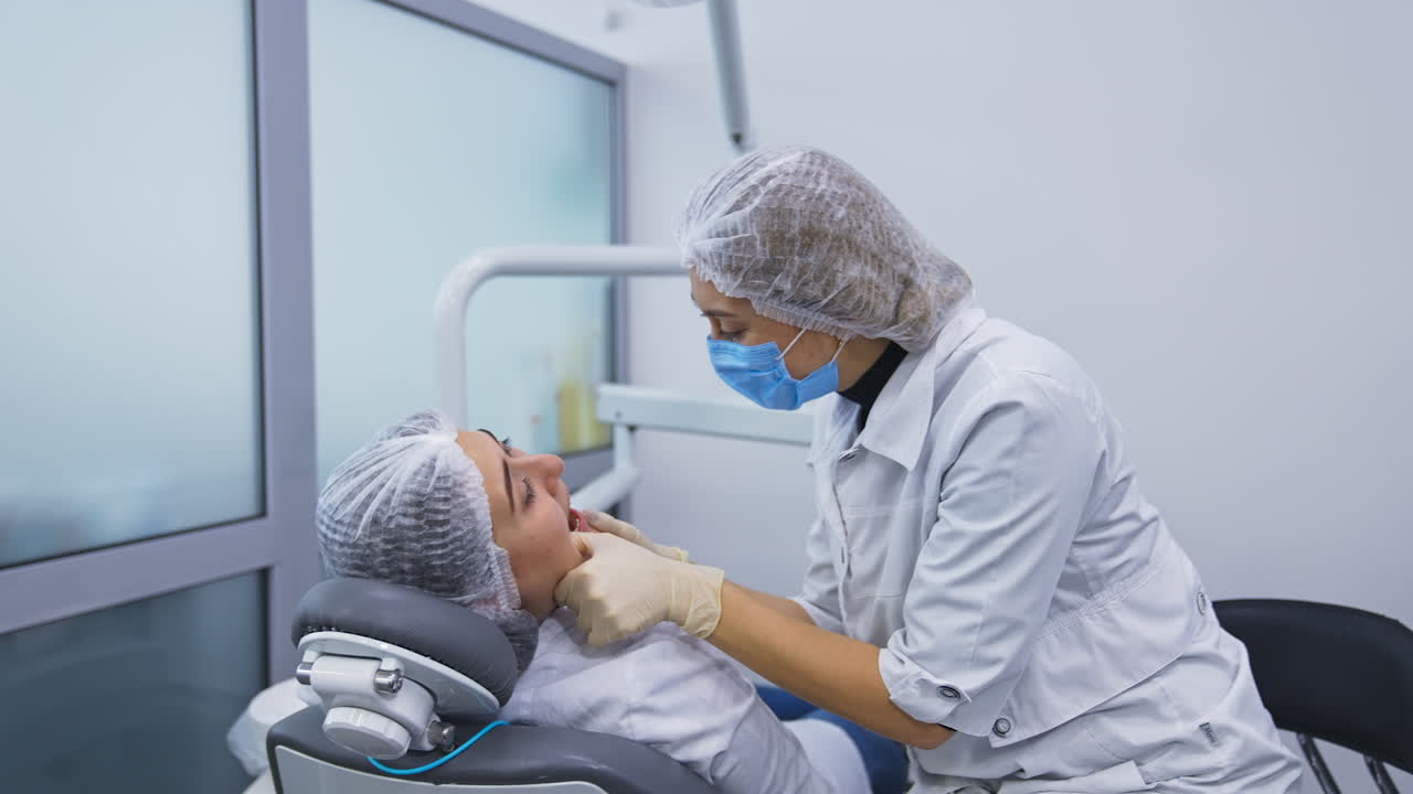 Two female students are practicing on each other. Woman holds the lower jaw of a patient and looks attentively on teeth.