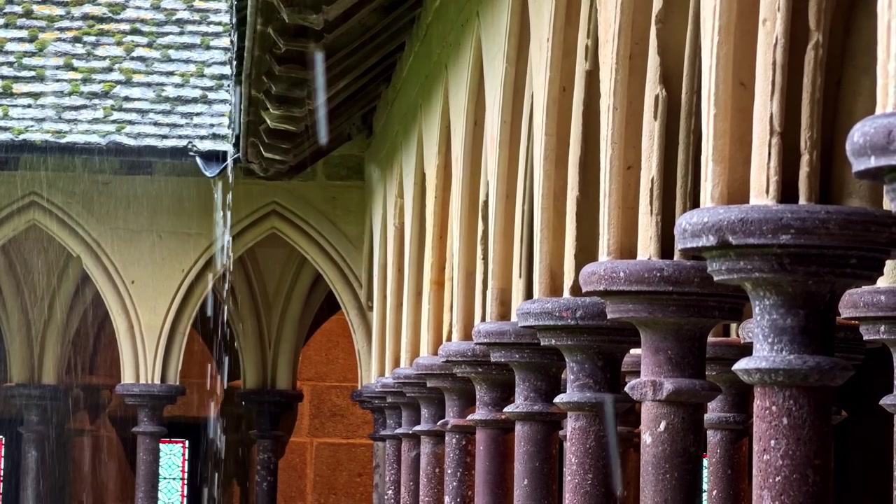 L'acqua piovana scorre dal tetto del chiostro di Mont-Saint-Michel, mettendo in risalto le colonne architettoniche. Ideale per documentari storici e studi architettonici.