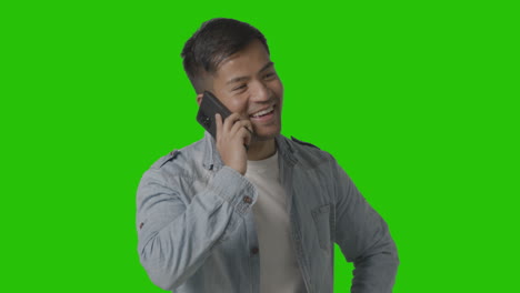 Studio-Shot-Of-Casually-Dressed-Smiling-Young-Man-Talking-On-Mobile-Phone-Against-Green-Screen-