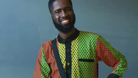 close-up view of young cheerful african american man in traditional clothes playing a drummer and smiling at camera