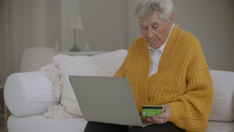 online shopping and people concept - happy senior woman with laptop computer and credit or bank card at home. old woman shopping with a credit card and a laptop