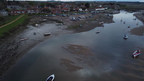 aerial drone shot flying over creek at low tide with sailing boats and boathouse in burnham overy staithe north norfolk on cloudy gloomy moody day uk