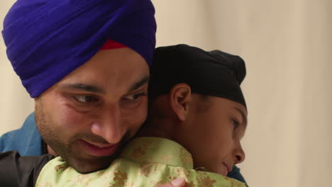 close up studio shot of sikh father embracing son both wearing turbans against plain background 5