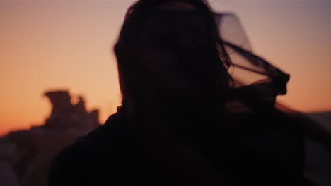 A-girl-holding-a-black-scarf-in-her-hand-over-a-rock-in-the-desert-wearing-an-abaya-while-sunset-close-up-shot-fossil-dunes