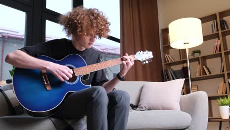 a male musician plays a blue acoustic guitar. modern young hipster guitarist playing guitar. stylish curly hair.