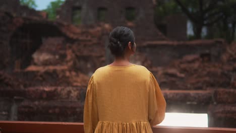 A-woman-in-a-yellow-dress-stands-in-front-of-ancient-ruins,-contemplating-the-history-around-her