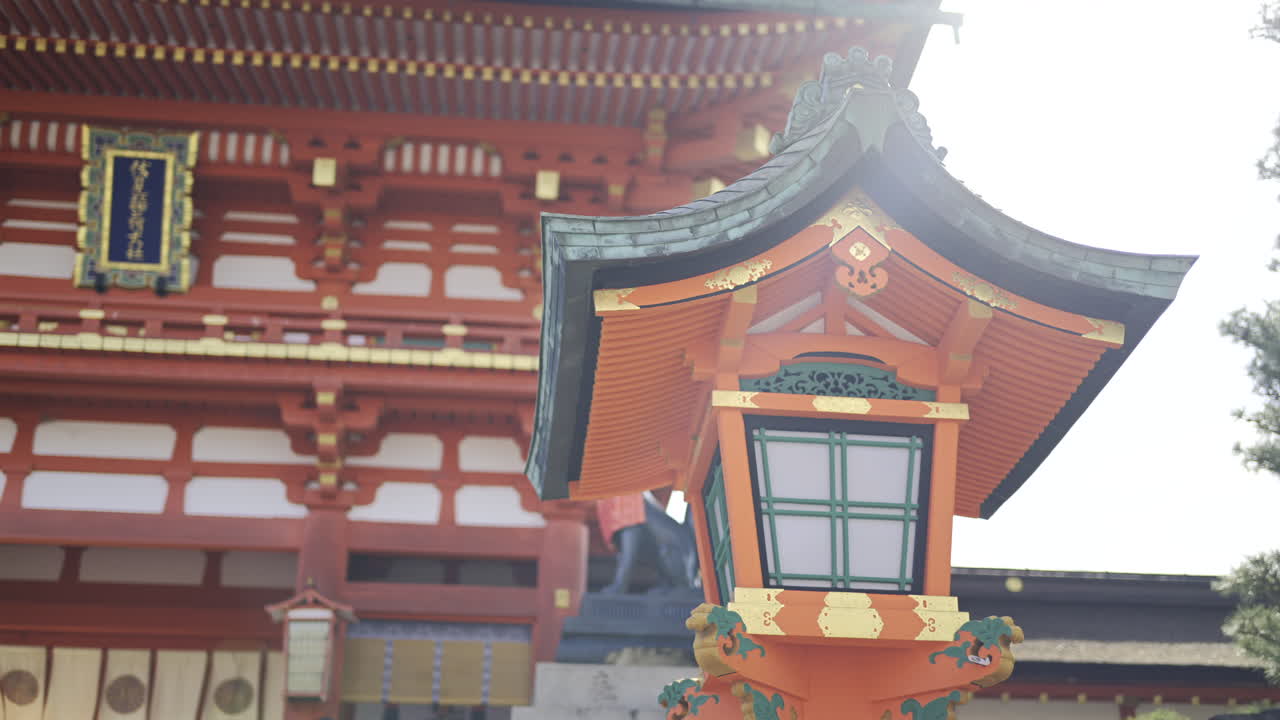 Admire the stunning details of traditional Japanese architecture, featuring a beautifully crafted lantern and an iconic Fushimi Inari shrine against a clear blue sky. Kyoto, Japan