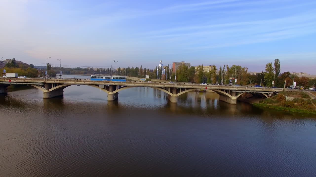 Public and private transport moving along the bridge over the river. Drone footage rising over the city on sunny autumn day.