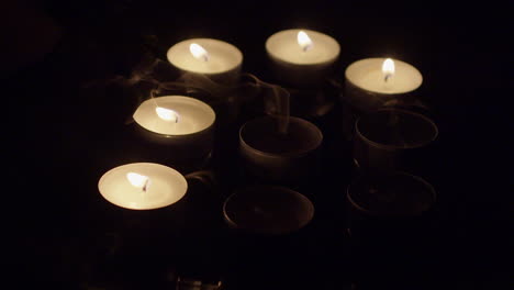 grupo de velas de té encendidas en una bandeja reflectante soplada a la oscuridad