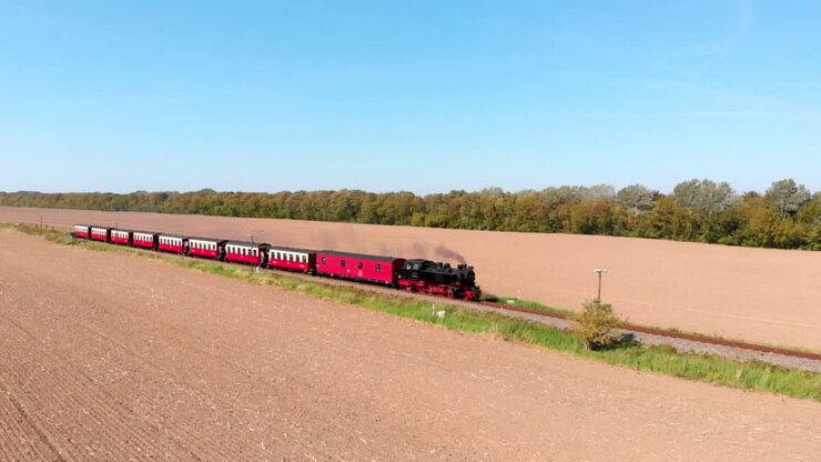 Aerial: steam narrow gauge railway in the countryside passing by sown fields