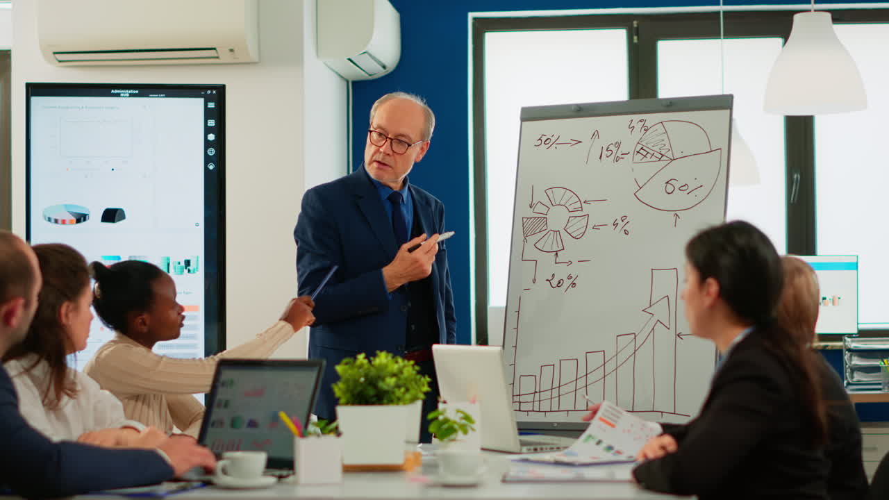 Senior businessman in eyeglasses and formal suit drawing financial plan on flipchart