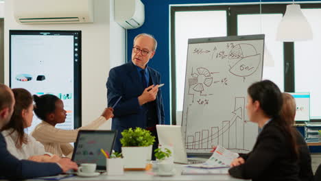 senior businessman in eyeglasses and formal suit drawing financial plan on flipchart