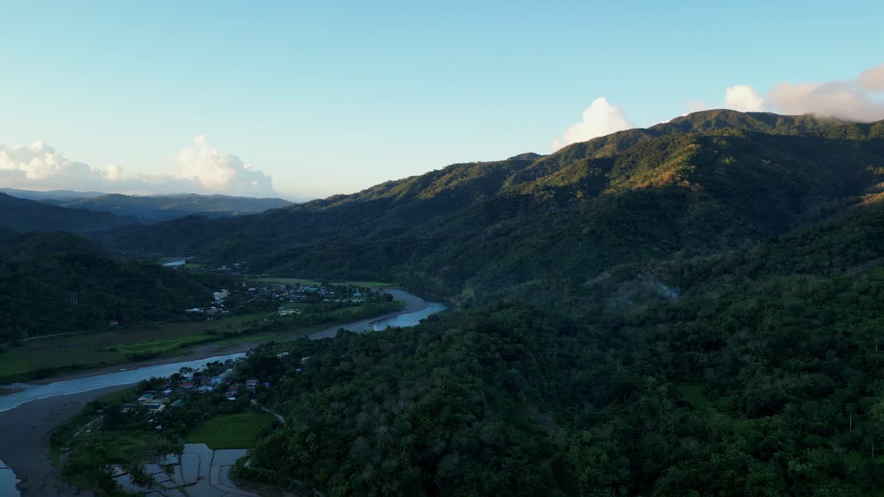 Panoramic aerial overview of lush tropical jungle valley with a meander river and sun setting against mountain peaks in San Miguel, Catanduanes.