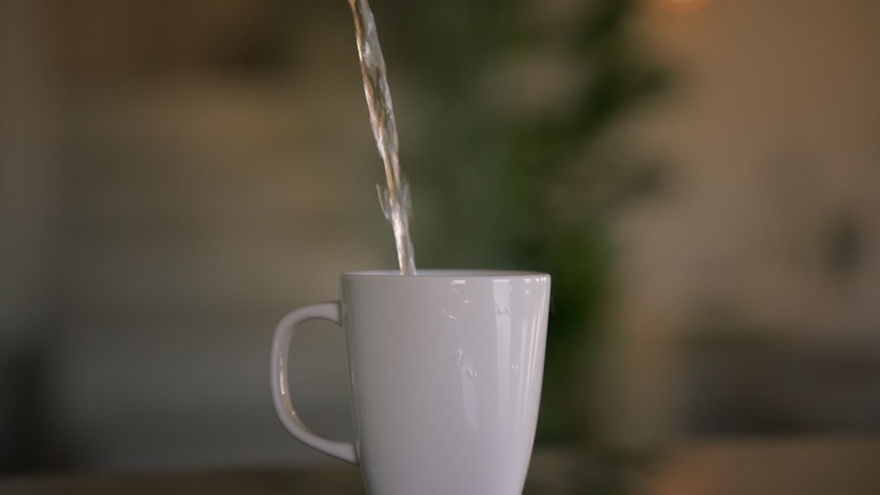 agua hirviendo caliente vertida en una taza blanca con asa, preparando té en la mesa