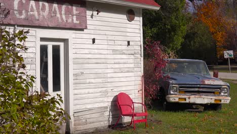 Eine-Attraktive-Alte-Verwitterte-Garage-Entlang-Einer-Landstraße-In-Amerika-Mit-Einem-Verlassenen-Pickup-Truck