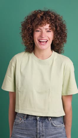 smiling standing young curly haired woman on green background. vertical orientation