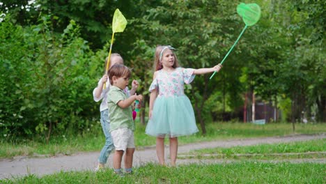 happy children in the park in a warm sunny day. two little girls holding butterfly nets. cute little boy with bubble blower outdoors. happy childhood.