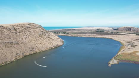 aerial view of deep-blue lake, coastline, volcanic peninsula and power boats racing around course - lake forsyth