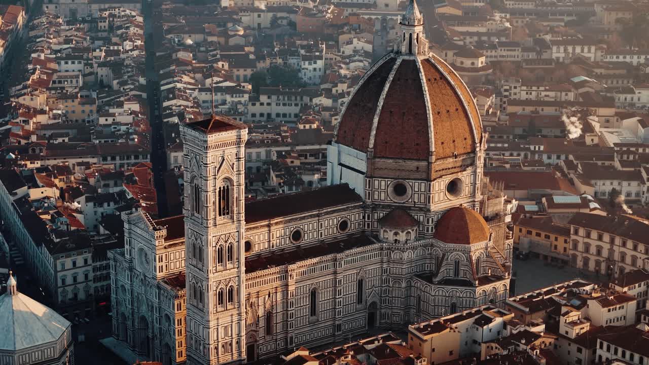 Aerial medium pullback from Florence Duomo at sunrise, revealing warm golden hues on dome and tower and the historic skyline
