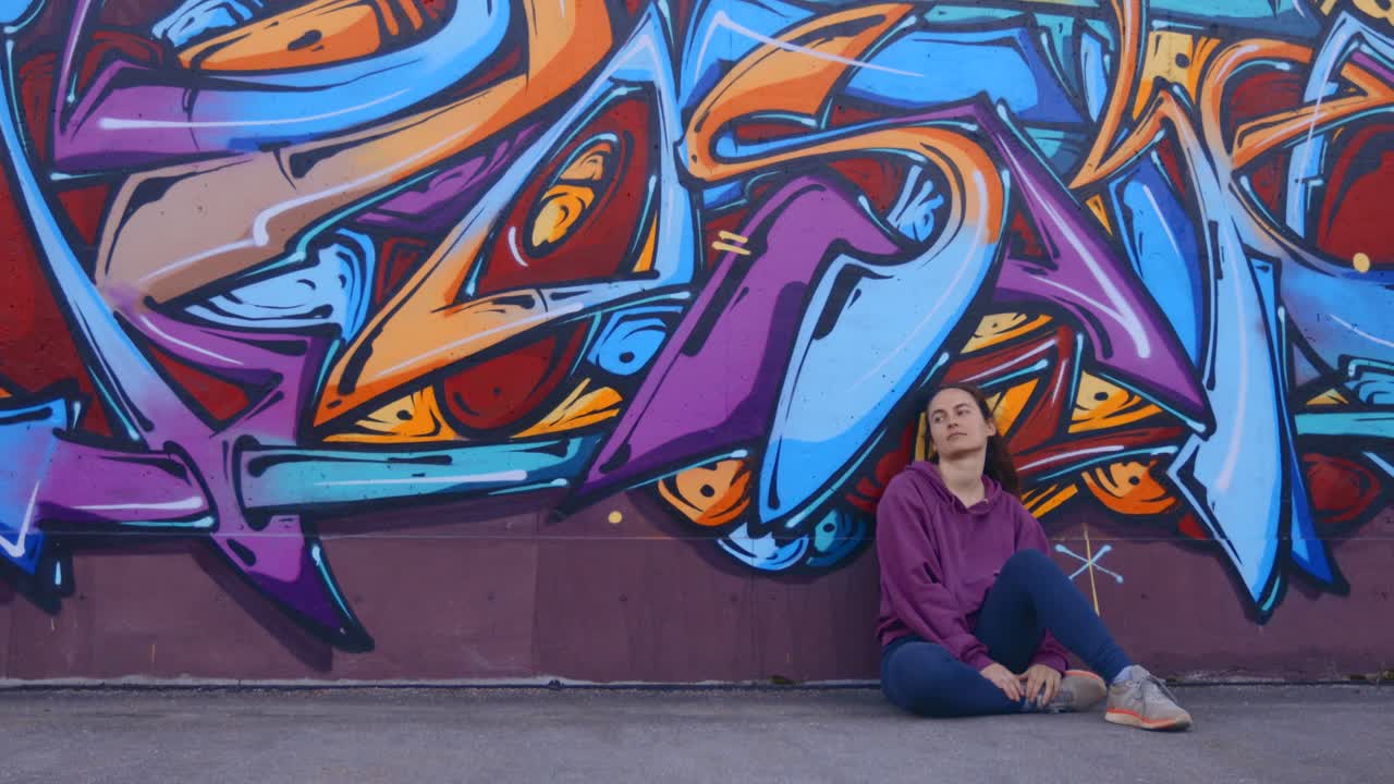 Una donna seduta davanti a un muro di graffiti colorati, in contemplazione.