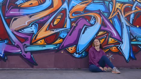 a woman sitting in front of a colorful graffiti wall, contemplating