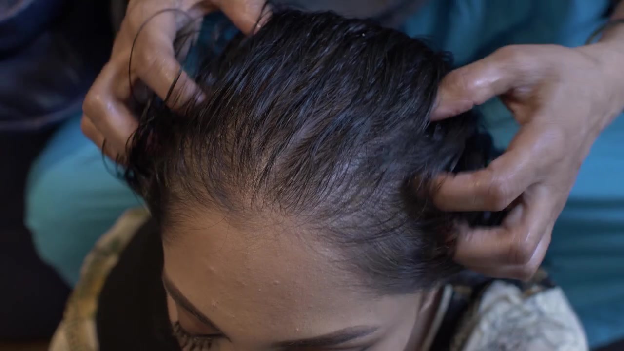 Jovem mulher asiática recebendo massagem com óleo no couro cabeludo e cabelo. Vista superior, câmera fixa.