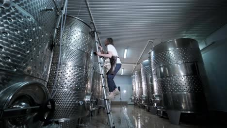 un agricultor o viticultor feliz está caminando en medio de tanques de vino y comprobando un grado de fermentación de la producción de vino de alta calidad en una instalación moderna de elaboración de vino o bodega.