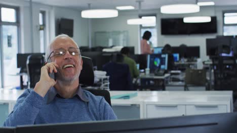 Man-talking-on-smartphone-while-sitting-on-his-desk-at-office